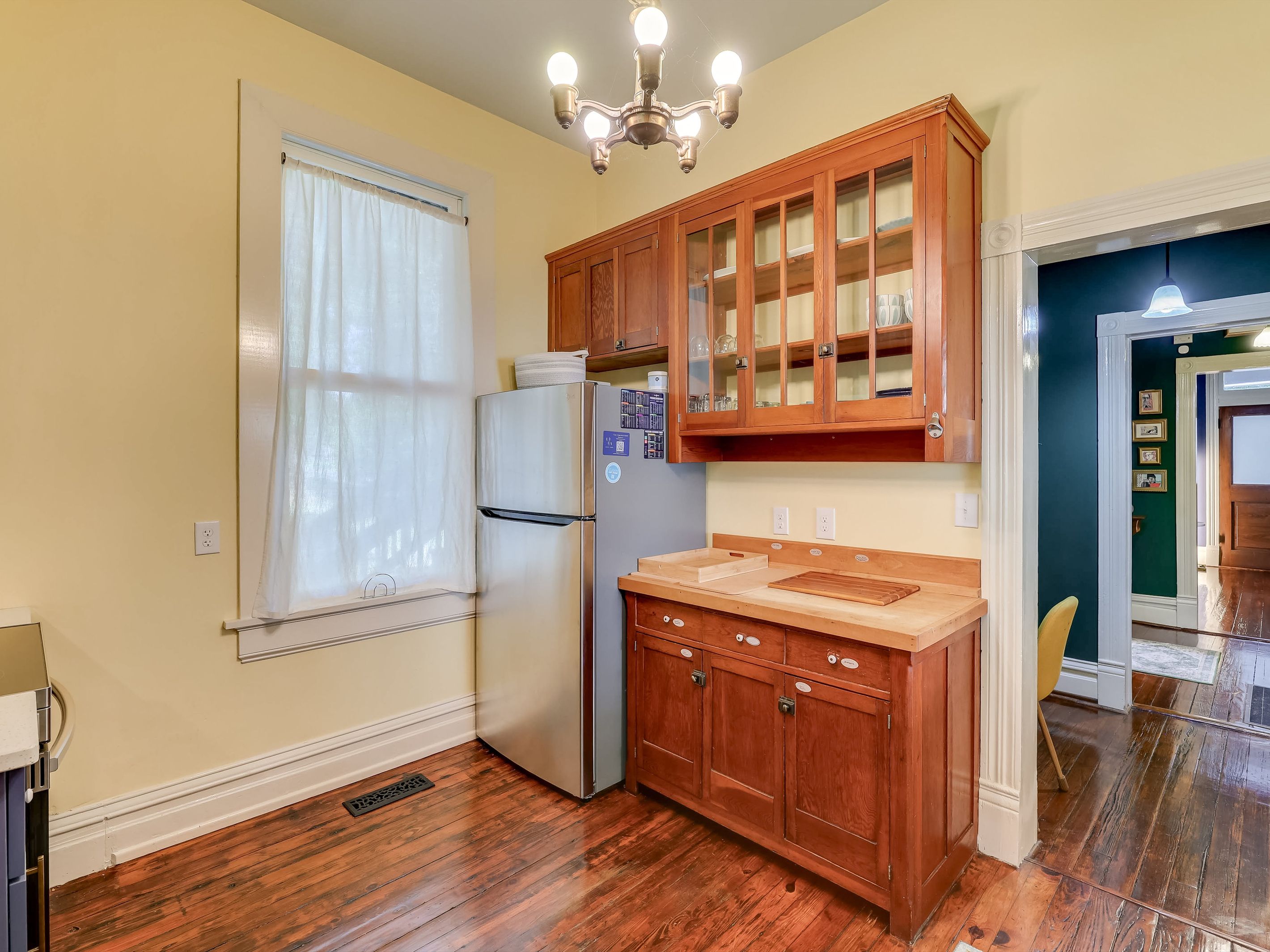 Una cocina con armarios de madera, un refrigerador de acero inoxidable y una ventana con cortina blanca.