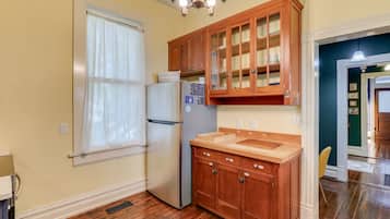Una cocina con armarios de madera, un refrigerador de acero inoxidable y una ventana con cortina blanca.
