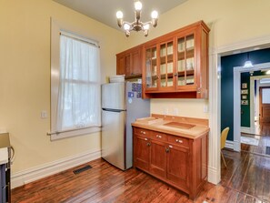 A kitchen with wooden cabinets, a stainless steel refrigerator, and a window with a white curtain.