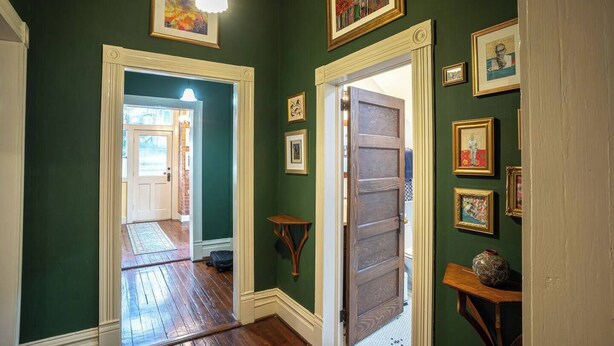 Un pasillo con paredes verdes, suelo de madera y una puerta que da a otra habitación.