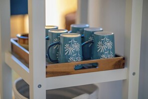 Een houten plank met zes smaragdgroene mokken met witte bloemmotieven.