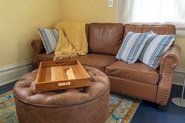 Een bruine leren bank met gekleurde kussens, een houten dienblad en een decoratieve plaid.