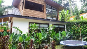 Une maison à deux étages dotée d’un balcon, entourée d’une végétation tropicale luxuriante.