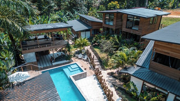 Un complexe hôtelier moderne doté d’une piscine, de chalets en bois et d’une végétation tropicale luxuriante.