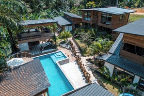 Un moderno resort con piscina, cabañas de madera y exuberante vegetación tropical.