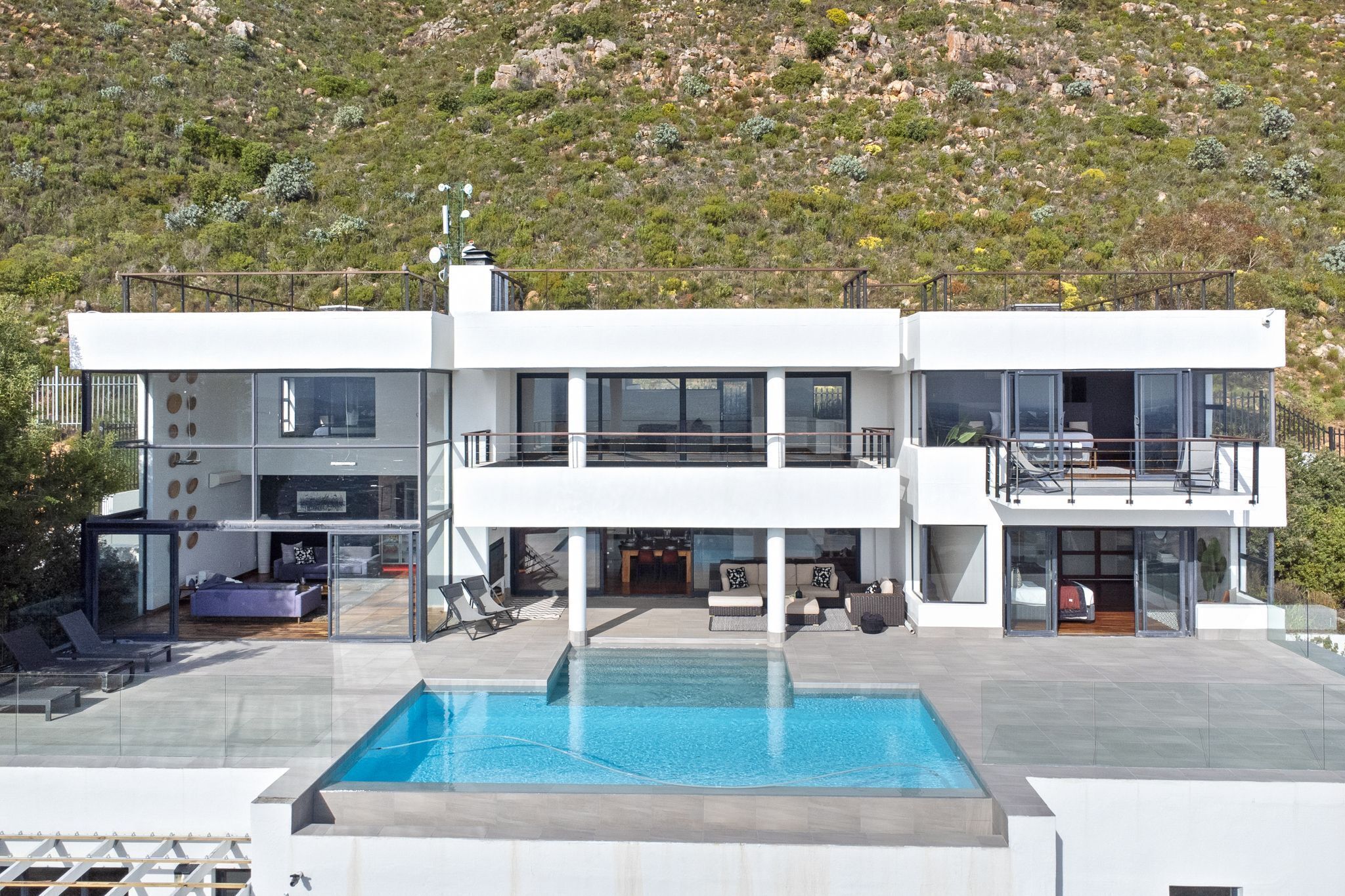 Una casa moderna de dos pisos con piscina, mobiliario exterior y vista a un paisaje montañoso.