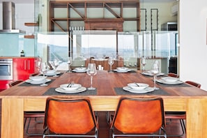 A dining area with a large wooden table set for six, surrounded by orange chairs, with a view through a glass partition. - Restio View 11 - Three Bedroom House, Sleeps 6 (Cape Town)