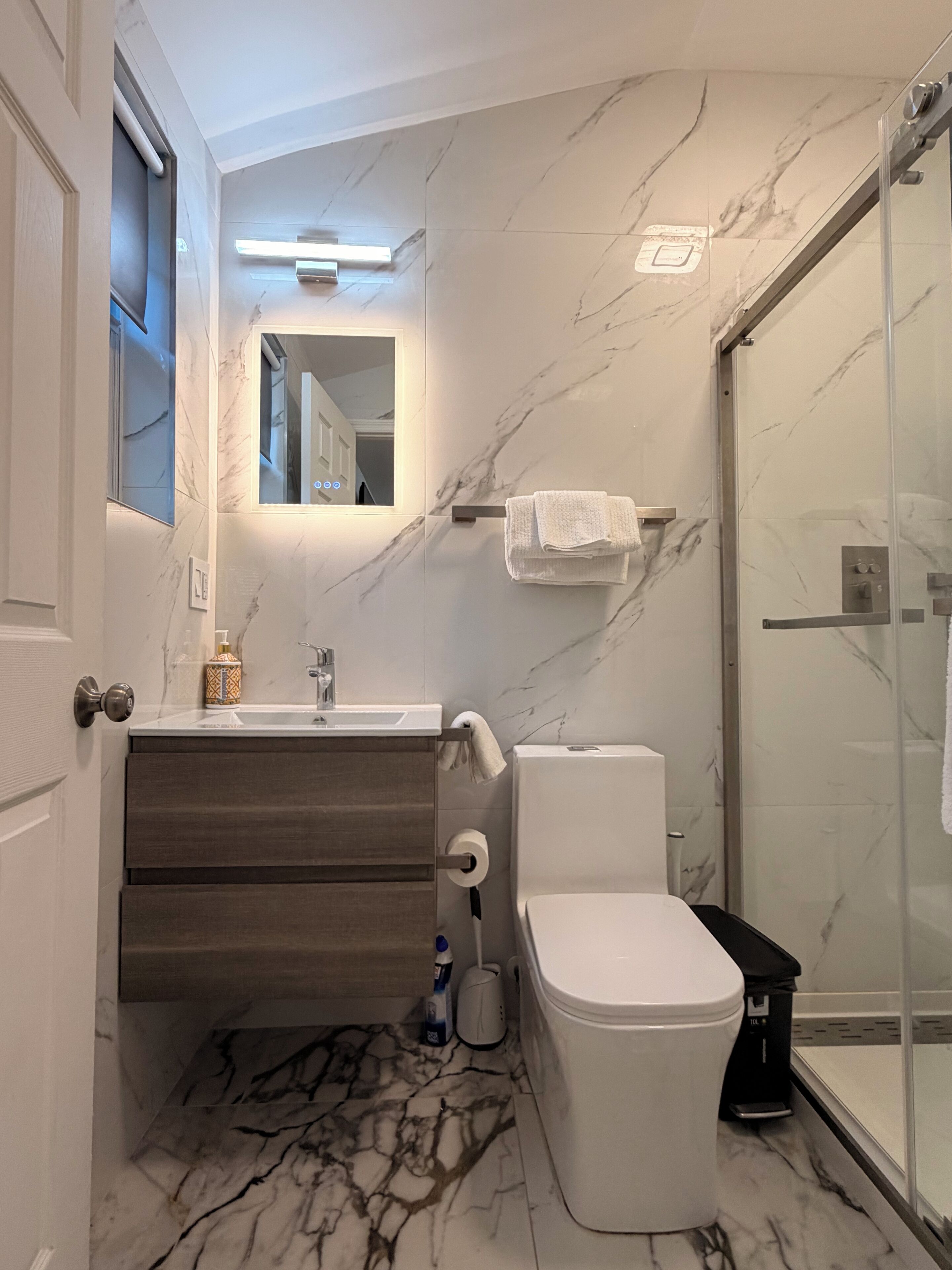 Casa de banho moderna com soalho em mármore, sanita branca, lavatório com espelho e cabine de duche em vidro.