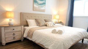 A bedroom with a large bed, two bedside tables with lamps, a headboard, and a painting on the wall.