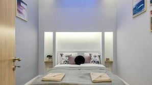 Een keurig opgemaakt bed met hoofdeinde, twee nachtkastjes met lampen, en een deur aan de linkerkant.