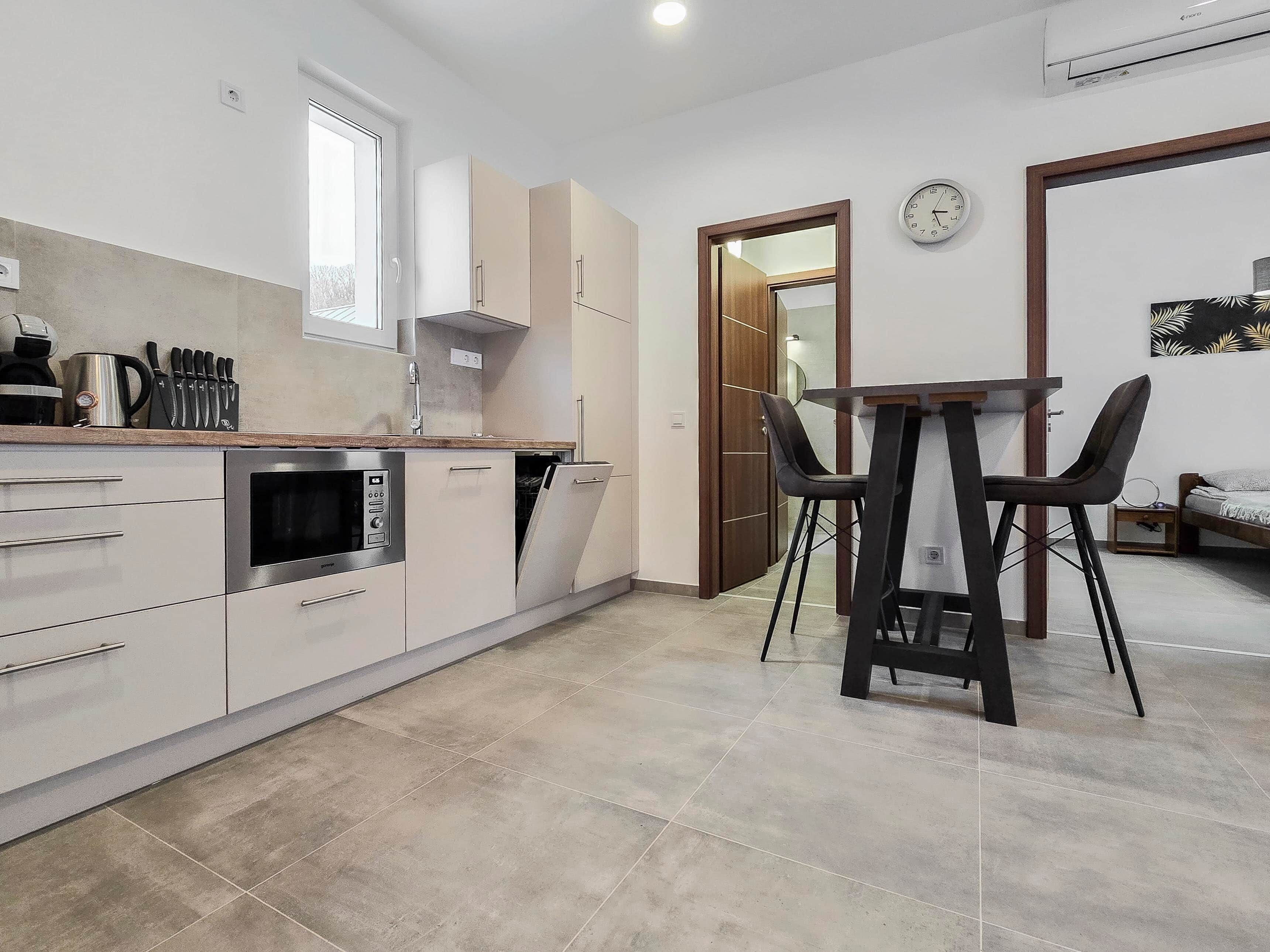 A modern kitchen with a built-in oven, a dishwasher, and a dining area with a table and chairs.