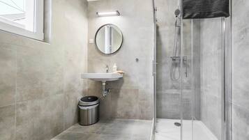 A modern bathroom with a glass-enclosed shower, a sink with a mirror above it, and a trash bin.