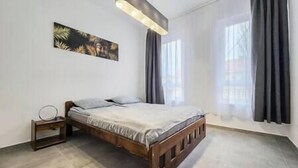 Une chambre à coucher avec un lit en bois, une table de chevet, un luminaire suspendu et une grande fenêtre avec des rideaux.