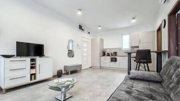 Un salon moderne avec un canapé gris, une table basse en verre et un téléviseur à écran plat posé sur un meuble blanc.