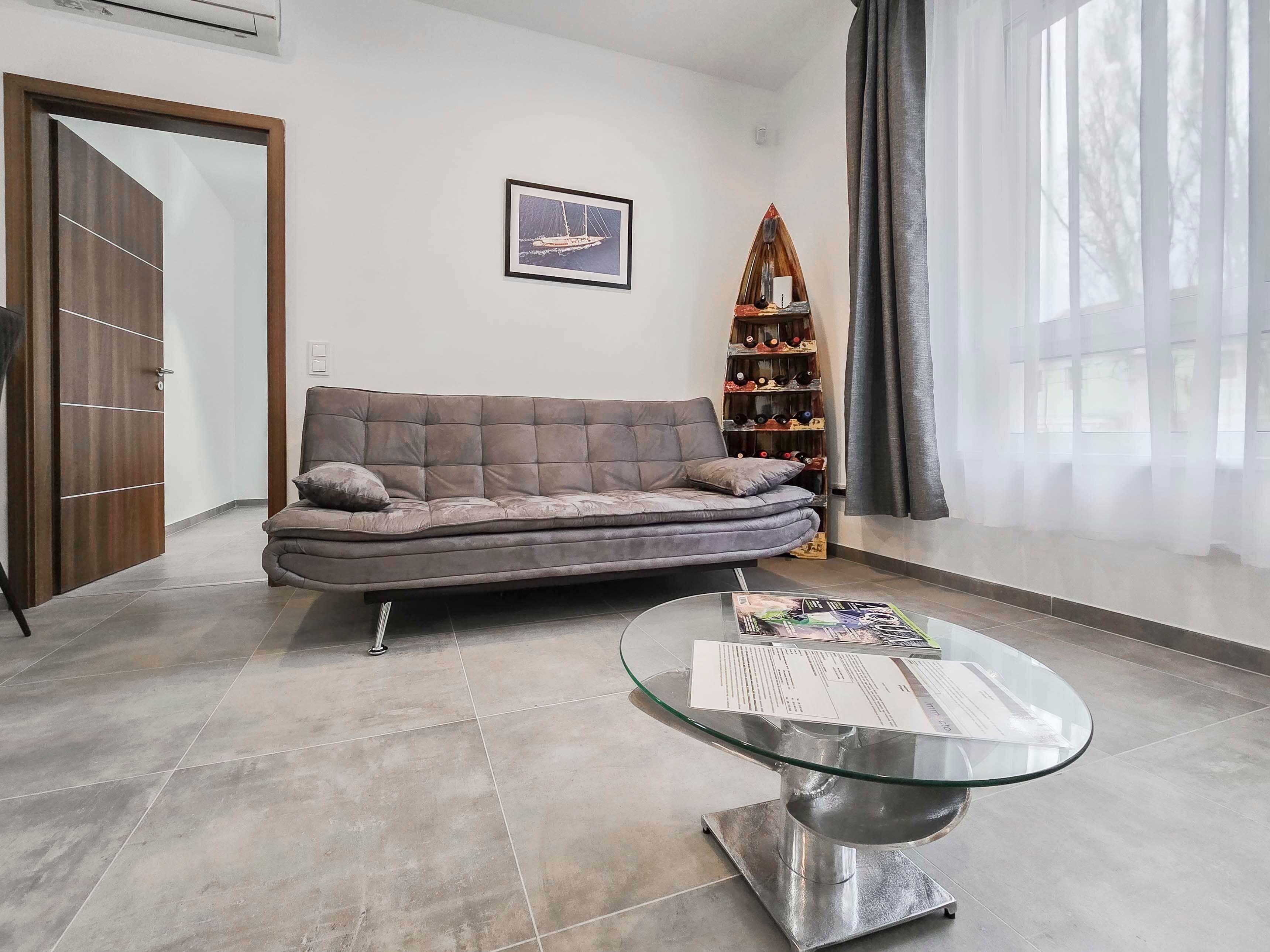 A modern living room with a sofa, a glass coffee table, a wine rack, and a door.