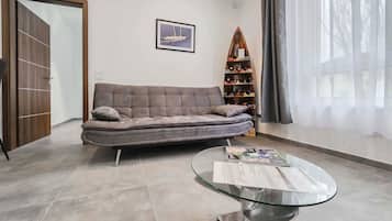 A modern living room with a sofa, a glass coffee table, a wine rack, and a door.