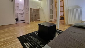 A room with a wooden floor, a black ottoman, a bed, a ladder, and a radiator. - MidTerm - Pody Apartment Budapest (Budapest)