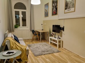 A compact living space with a sofa, a small table, a TV, and a desk. - MidTerm - Pody Apartment Budapest (Budapest)