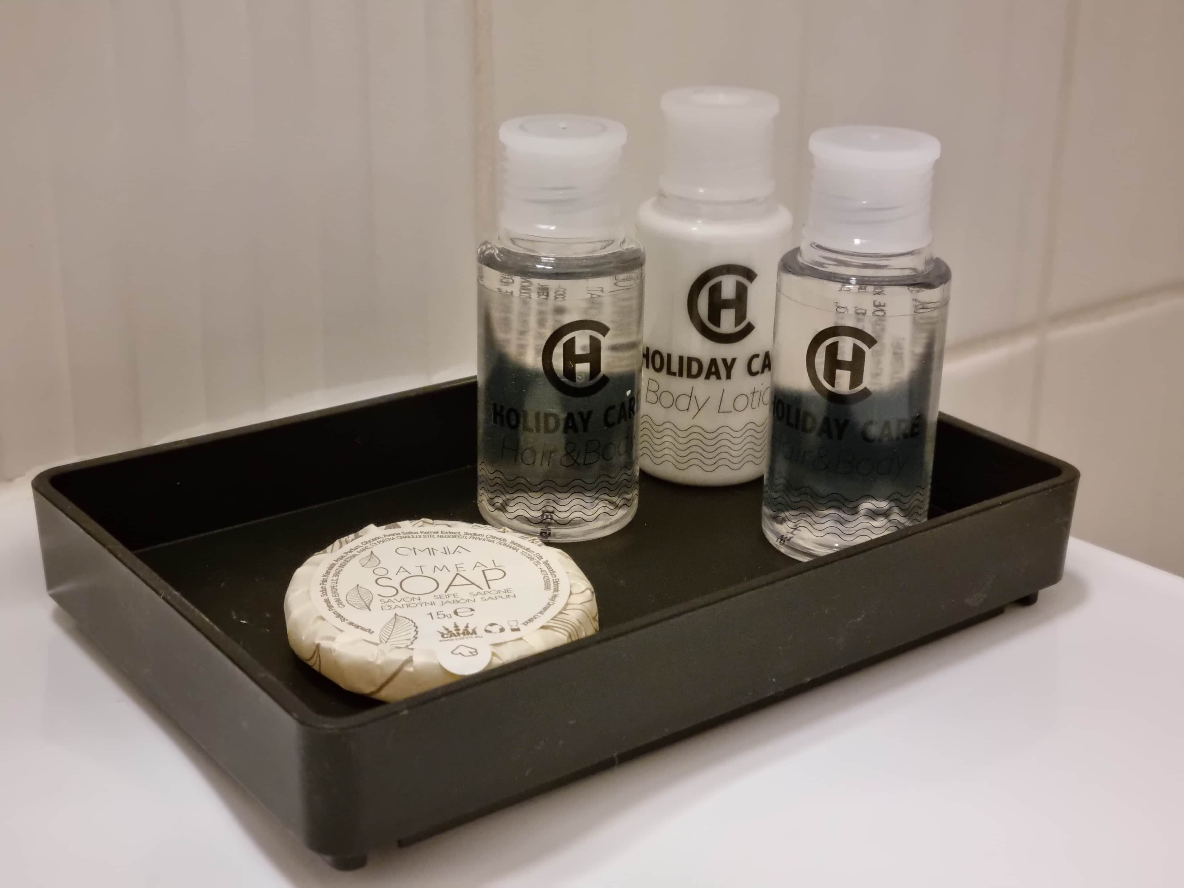 A black tray with three bottles of Holiday Care body lotion and a bar of soap.