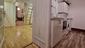 A modern kitchen with a microwave, oven, and washing machine. A wooden ladder is leaning against a white door. - MidTerm - Pody Apartment Budapest (Budapest)