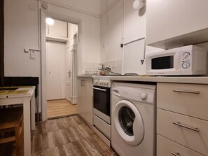 A compact kitchen with a washing machine, microwave, and a small dining area with a table and chairs. - MidTerm - Pody Apartment Budapest (Budapest)