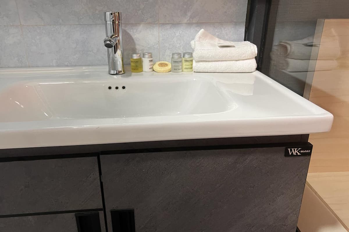 A bathroom with a white sink, a silver faucet, and a towel stacked on the side.