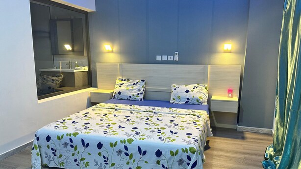 Una camera d'albergo moderna con un letto grande, comodini, una finestra e un bagno visibile attraverso la finestra.