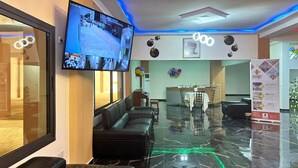 Hall d'albergo con una grande TV a schermo piatto montata a parete, una zona salotto con divani in pelle, un pavimento in marmo e una reception sullo sfondo.