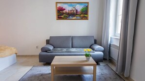 Een moderne woonkamer met een grijze bank, een houten salontafel en een schilderij van een kasteel aan de muur.