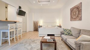 A modern bedroom with a bed, bedside tables, a TV mounted on the wall, a sofa, and a coffee table. - IMCT - Viktoria design studio apartment with A/C (Budapest)