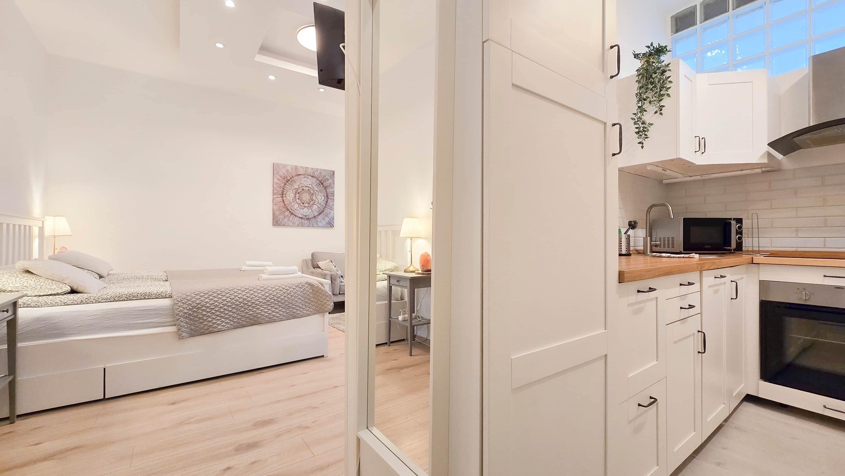 A modern apartment with a bed, bedside table, lamp, and a view of a kitchen area.