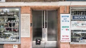 A storefront with a closed metal door, a signboard with contact information, and a Sony store in the background. - IMCT - Viktoria design studio apartment with A/C (Budapest)