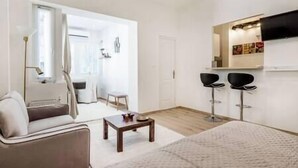 A modern living room with a sofa, a coffee table, and two black bar stools. - IMCT - Viktoria design studio apartment with A/C (Budapest)