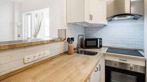 A modern kitchen with white cabinets, a wooden countertop, a microwave, a stove, and a window with curtains. - IMCT - Viktoria design studio apartment with A/C (Budapest)