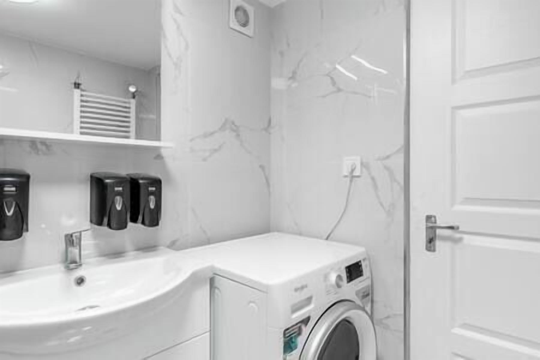 A modern bathroom with a white sink, a washing machine, and a towel rack.