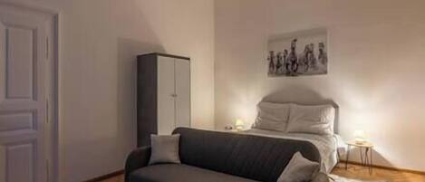Una camera da letto con un letto, un divano grigio, un armadio e un quadro appeso al muro.