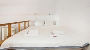 A neatly made bed with white linens and two towels, a wooden headboard, and a white wall.