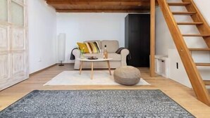 A living room with a wooden staircase, a sofa with cushions, a coffee table, and a patterned rug.