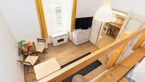 A compact living space with a wooden staircase, a small seating area with a table and chairs, and a window with curtains.