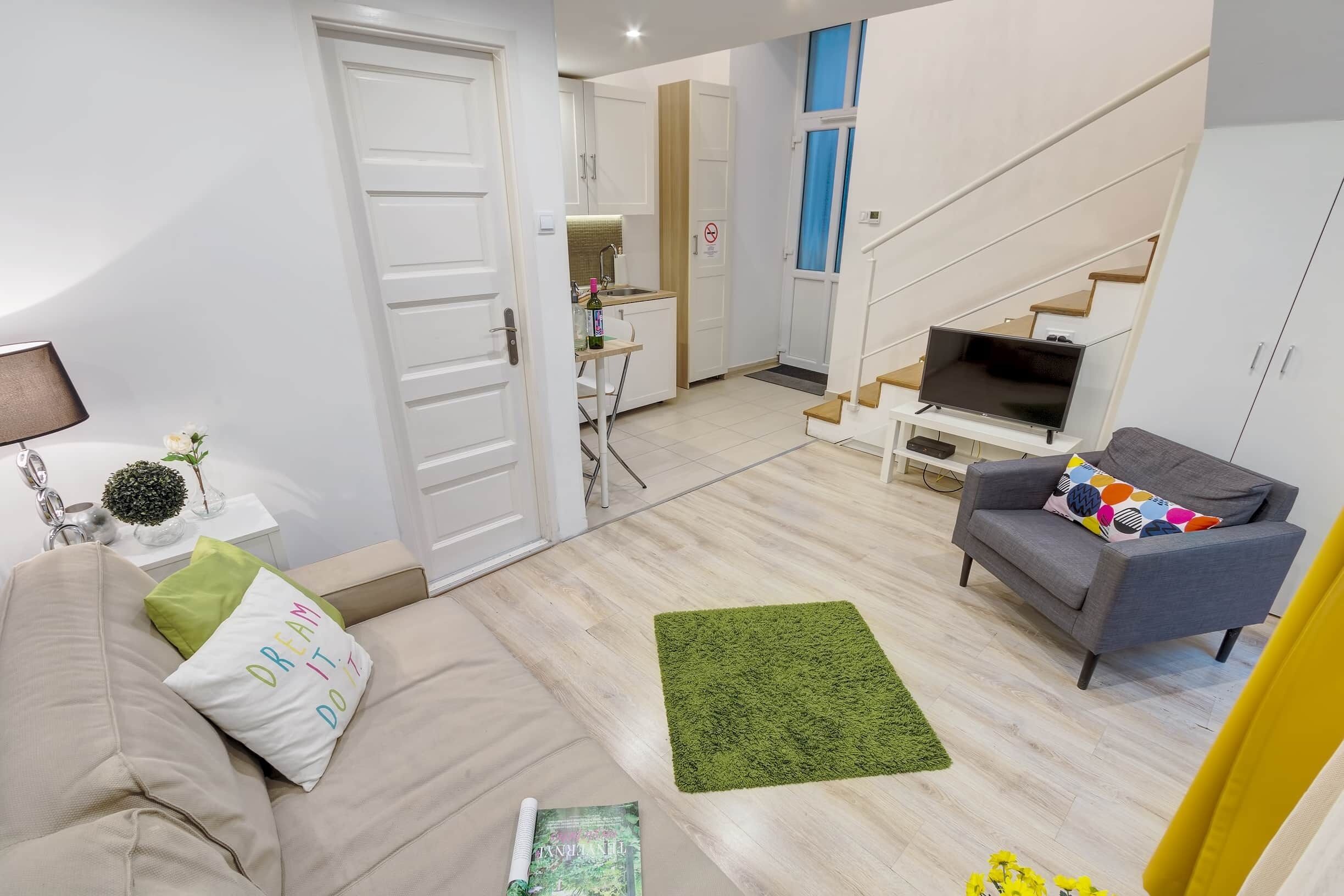 Ein modernes Wohnzimmer mit einer Couch, einem Fernseher und einer Treppe, die in einen Küchenbereich führt.