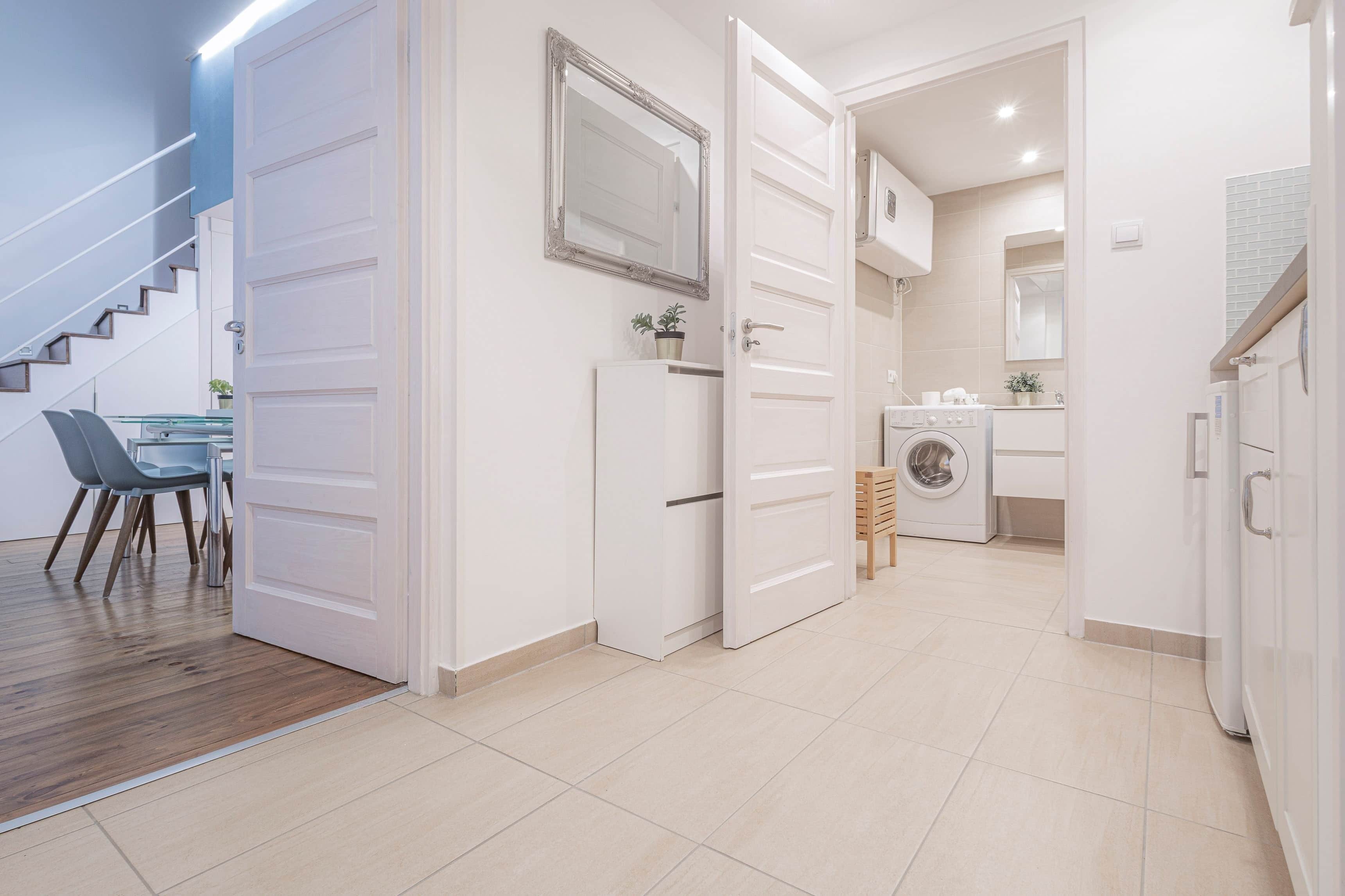 A modern interior with a staircase, a dining area with chairs, a kitchen with a washing machine, and a bathroom with a mirror.