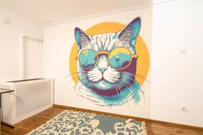 A room with a large wall mural of a cat wearing sunglasses, a radiator, a patterned rug, and a wooden floor. - Beautiful Home at Basilica 1 (Budapest)