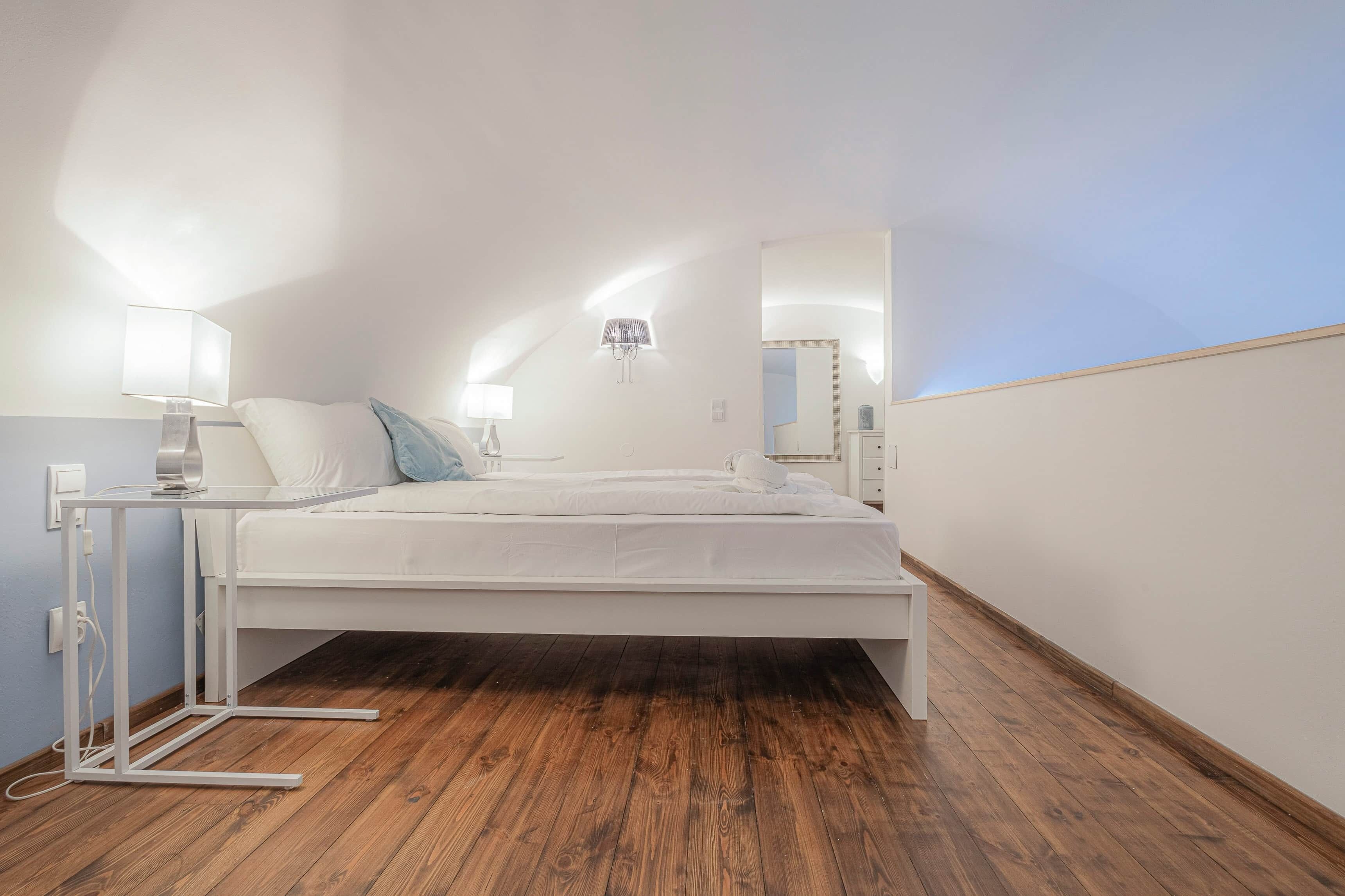 Une chambre à coucher avec un lit, des lampes de chevet, un luminaire fixé au mur et un plancher en bois.