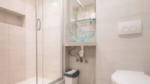 A modern bathroom with a glass shower enclosure, a glass sink, and a white toilet.