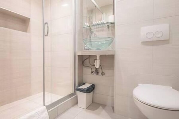 Et moderne badeværelse med brusekabine i glas, vask i glas og et hvidt toilet.