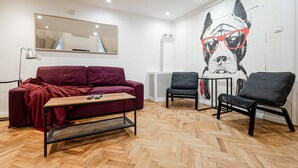 A modern living room with a herringbone wooden floor, a red sofa, two black chairs, a small wooden coffee table, and a wall-mounted mirror.