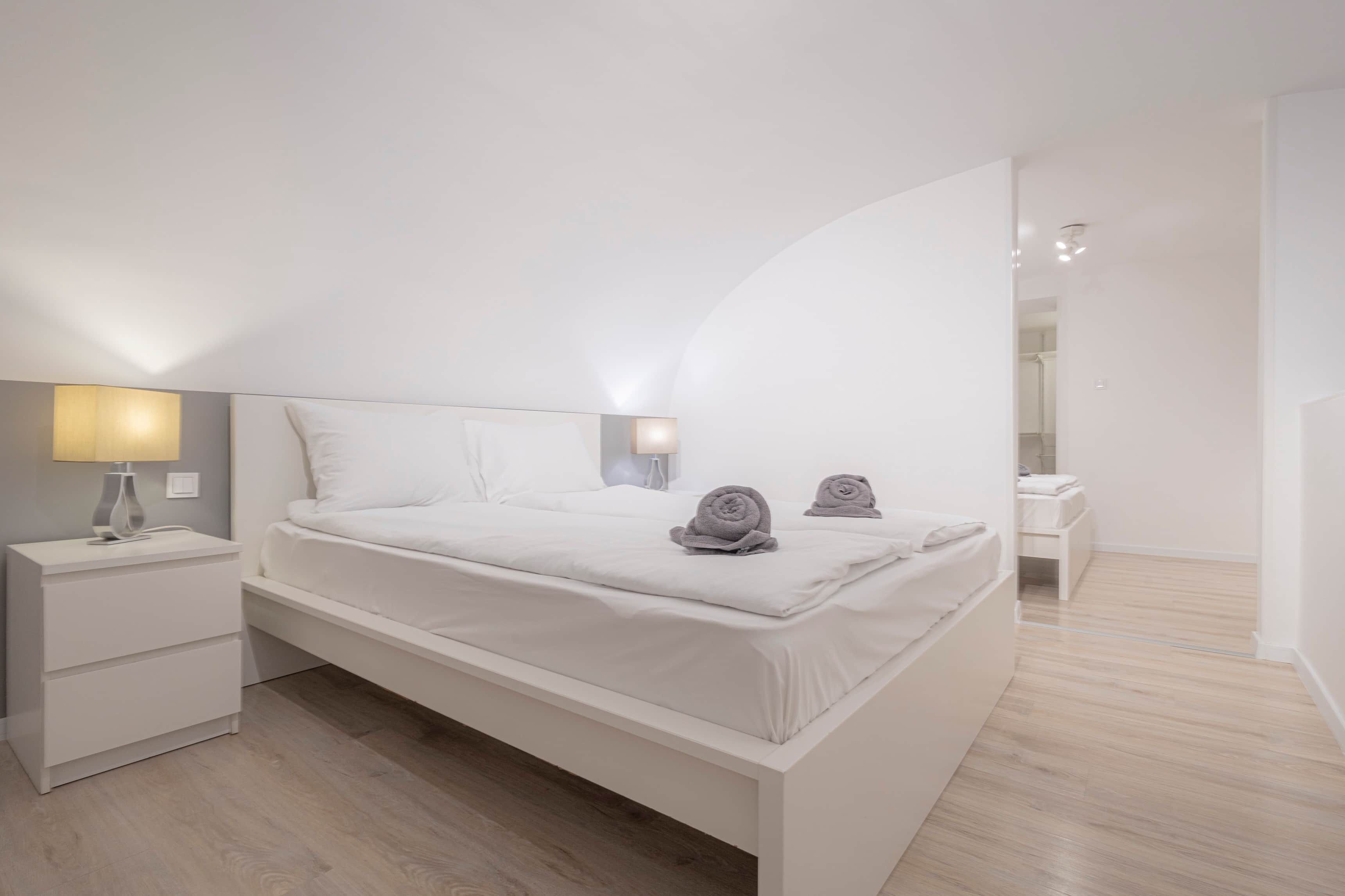 Une chambre à coucher moderne avec un lit, des tables de chevet, une lampe et une salle de bain à l’arrière-plan.