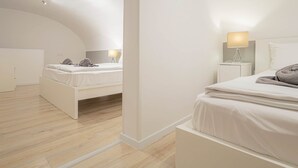 A modern, minimalist bedroom with two beds, a curved ceiling, and a wooden floor.