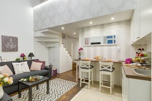 A modern apartment with a living area, kitchen, and a staircase leading to an upper floor.