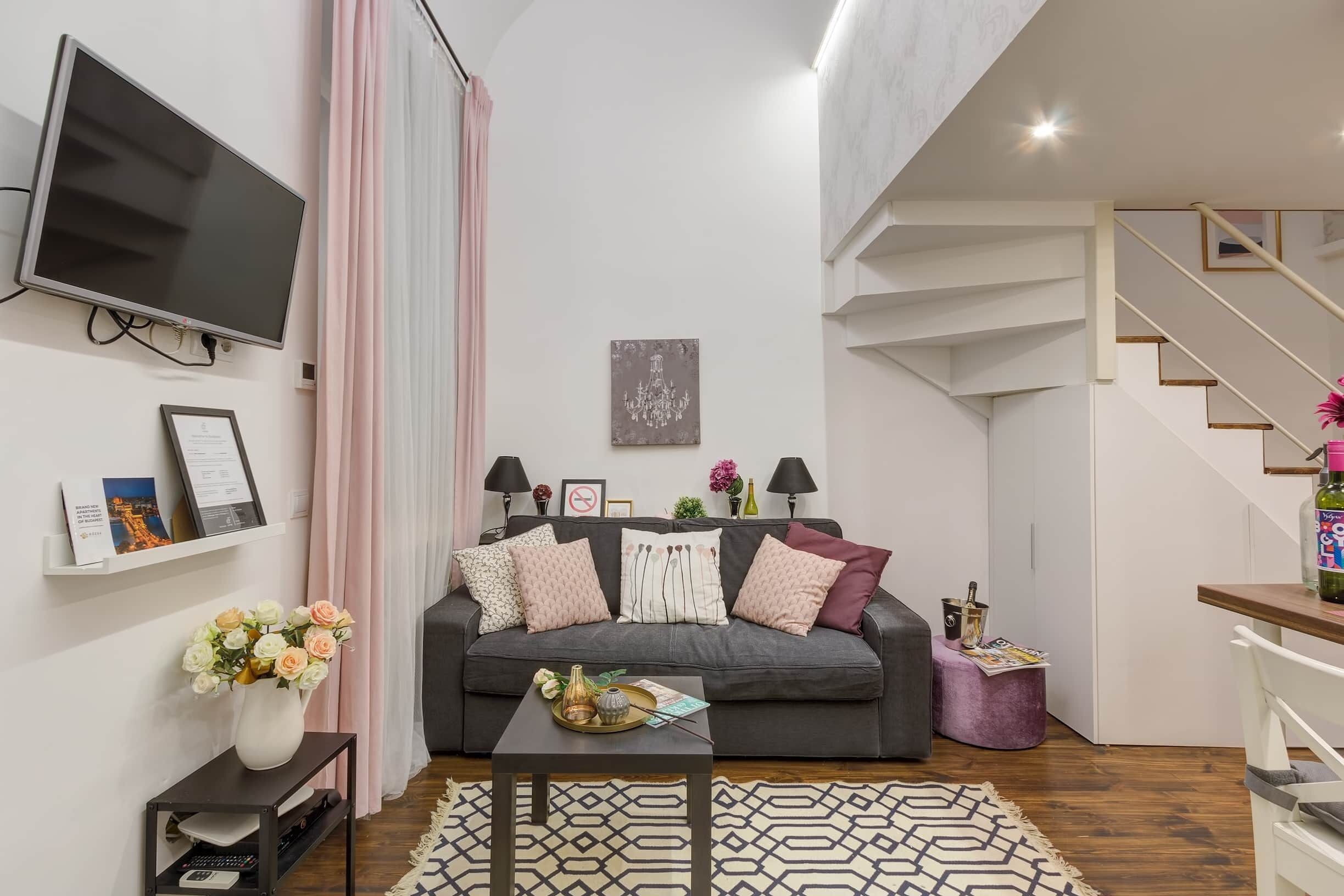 Un salon moderne avec un canapé gris, un téléviseur à écran plat, une table basse et un escalier.
